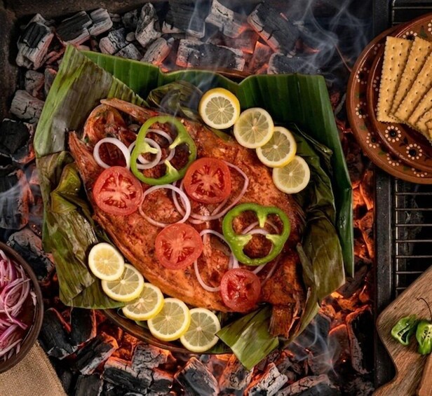 A whole fish on a banana leaf, garnished with slices of lemon, tomato, and green pepper, cooked over charcoal. 2