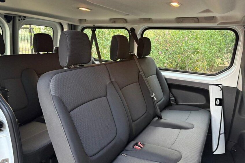 A vehicle interior with grey seats, a door, and a window showing greenery outside. 5