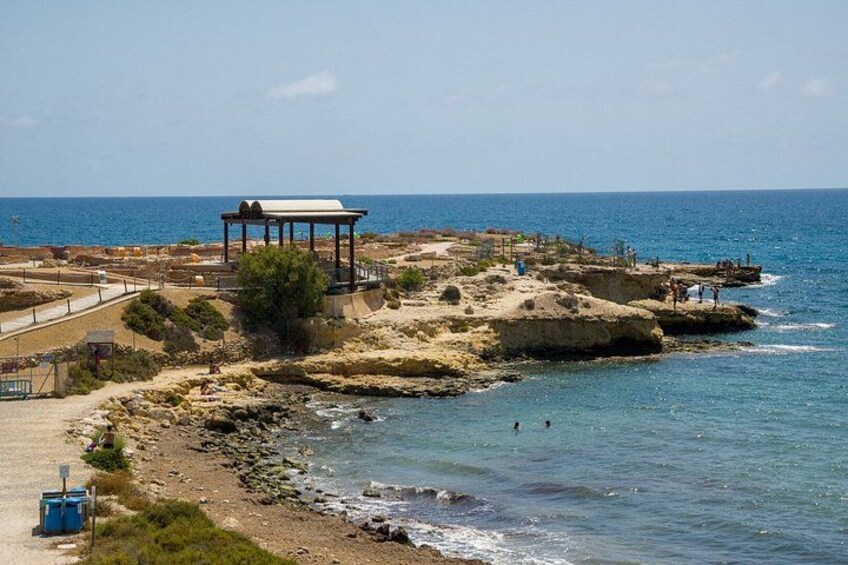 A coastal landscape with a rocky beach, a pavilion, and a clear blue sky. 3