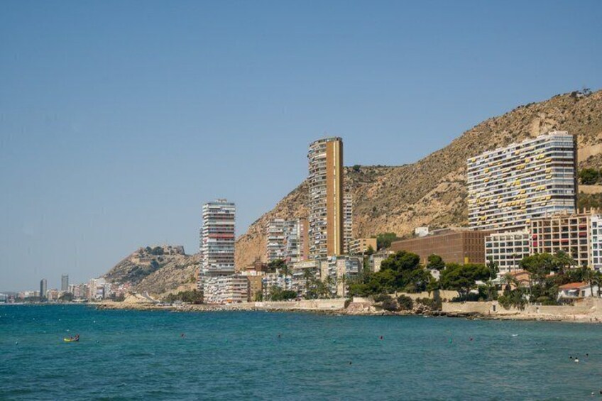 A coastal cityscape with high-rise buildings, a beach, and a hilly backdrop. 3