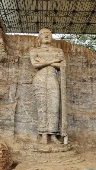 A large stone statue of a seated figure with crossed arms, set against a rocky background. 4