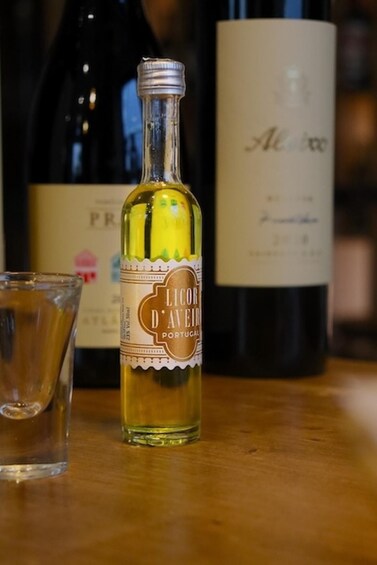 A bottle of Licoor d'Avéira Portugal wine, a glass, and another wine bottle in the background. 1