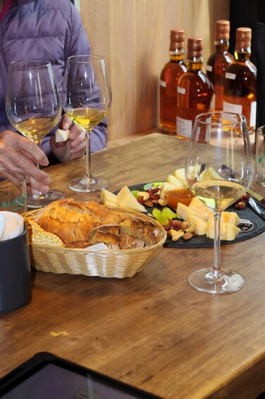 A table with wine glasses, cheese, nuts, and a basket of bread. 4