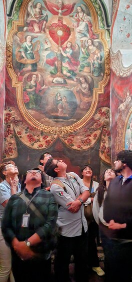 A group of people observing a large, ornate religious mural with figures and symbols. 1