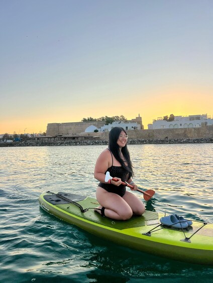A person sitting on a green kayak in calm water with a sunset in the background. 2
