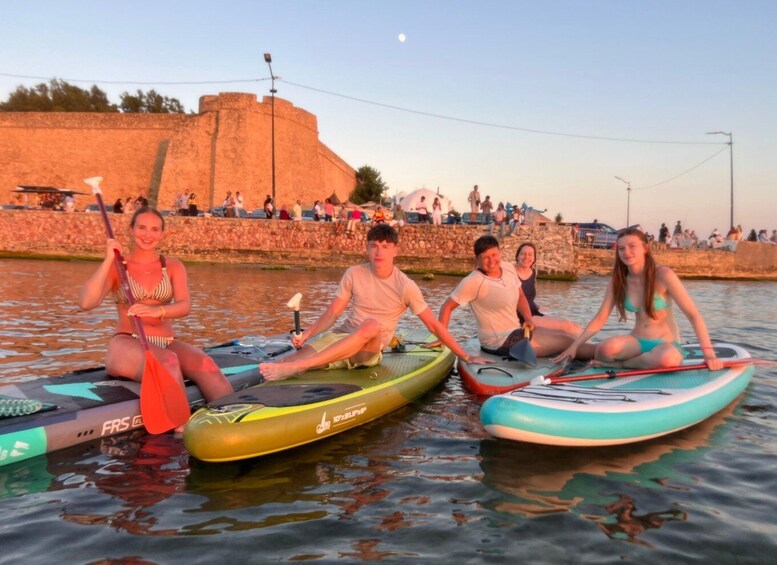 People sitting on paddleboards on water with a stone wall and a fort in the background. 5