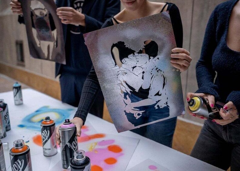 A person holding a spray-painted artwork, surrounded by cans of spray paint. 5