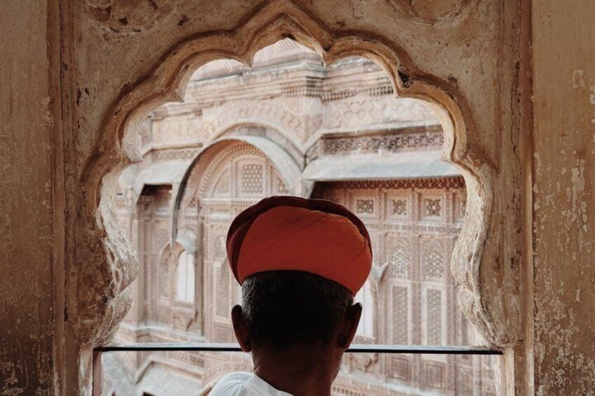 A person wearing a red cap looking through an arched window at a building with intricate patterns. 5