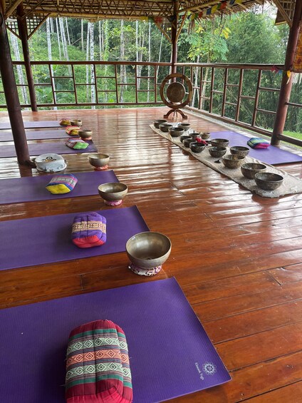 A wooden deck with yoga mats and meditation bowls arranged for a practice session. 2