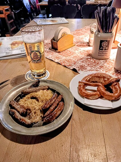 A table with a beer glass, a plate of sausages and sauerkraut, and a pretzel. 2