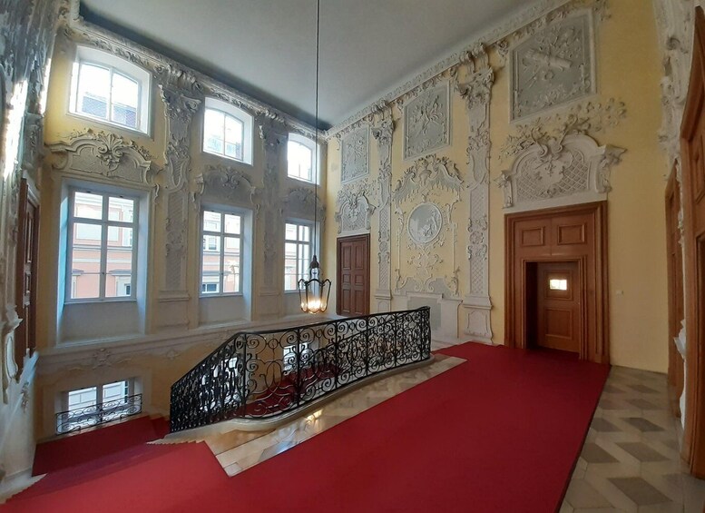 An ornate room with a red carpet, decorative moldings, and a staircase with a wrought iron railing. 4