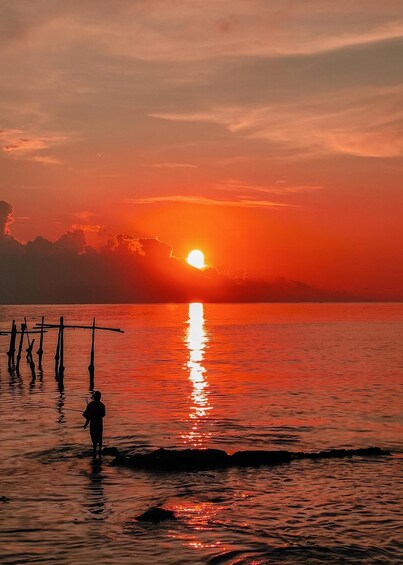 A sunset over a calm sea with a person standing on a dock. 1