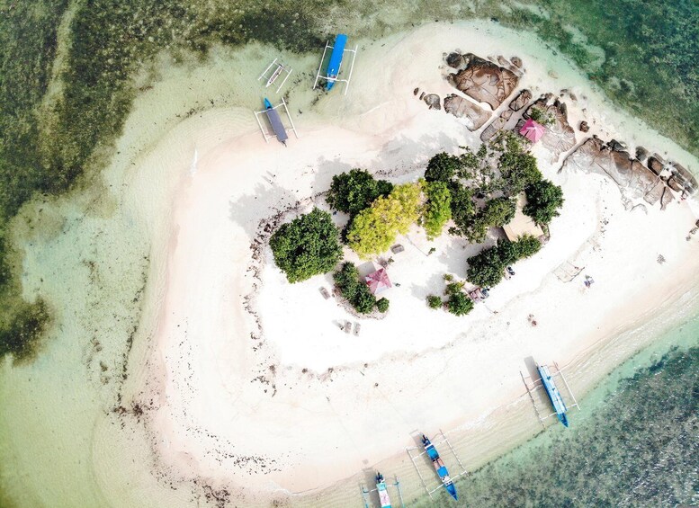 An aerial view of a small island with clear turquoise waters, surrounded by a white sandy beach, and several boats anchored near the shore. 4