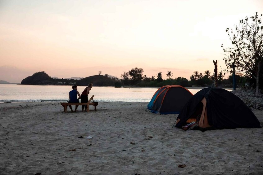 A beach with two tents and a bench where two people are sitting. 2