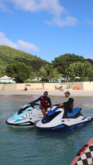 Two people on jet skis on a calm body of water with a beach and palm trees in the background. 5