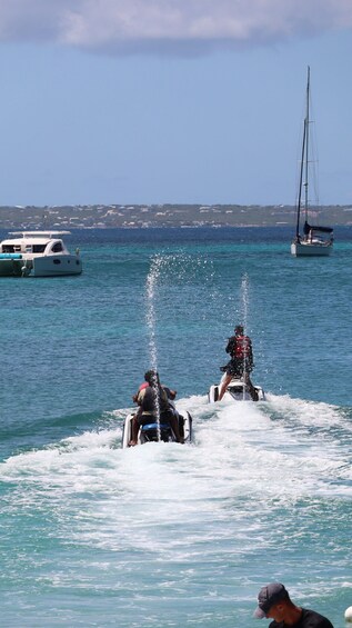 Two jet skis with water jets in the water, a sailboat, and a coastline in the background. 3