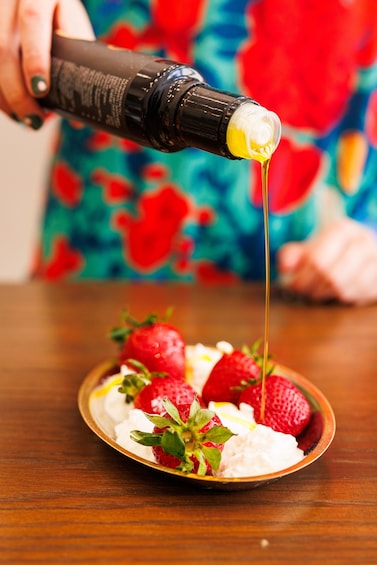 A person pouring a yellow liquid from a bottle onto a plate with strawberries and whipped cream. 2