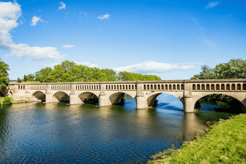 A stone bridge over a river with greenery on both sides. 1