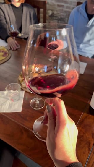 A hand holding a wine glass with red wine, a plate with food, and a table in a restaurant setting. 5