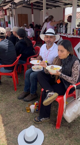 People seated on red plastic chairs outdoors, holding bowls of food and drinks. 4