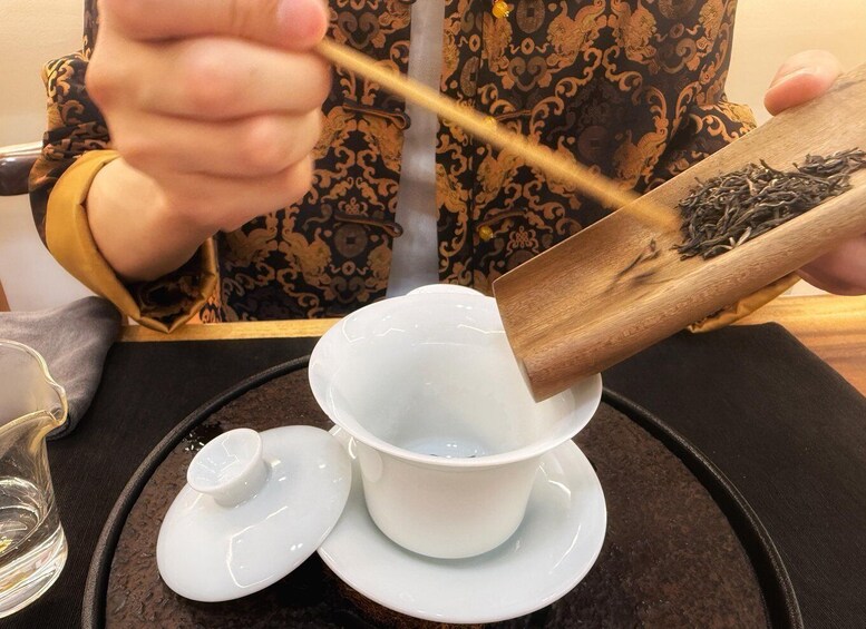 A person steeping tea leaves in hot water using a wooden tea infuser. 4