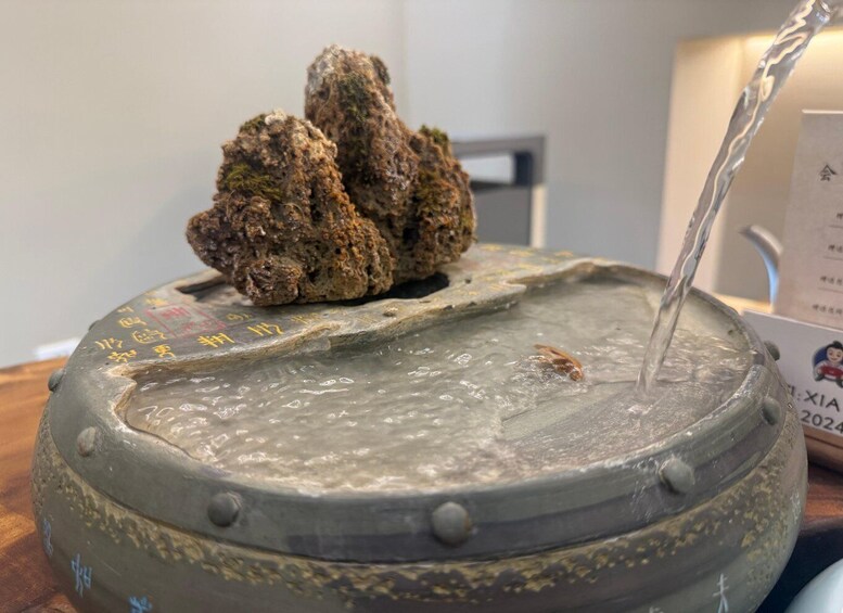 A stone basin with water flowing over it, featuring inscriptions and a moss-covered rock. 5