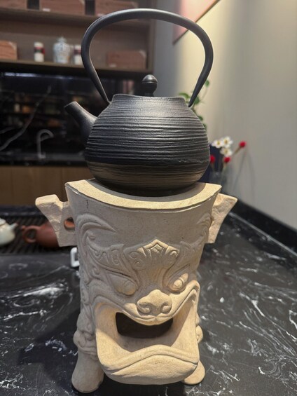 A black teapot on a ceramic stand with a carved face. 5