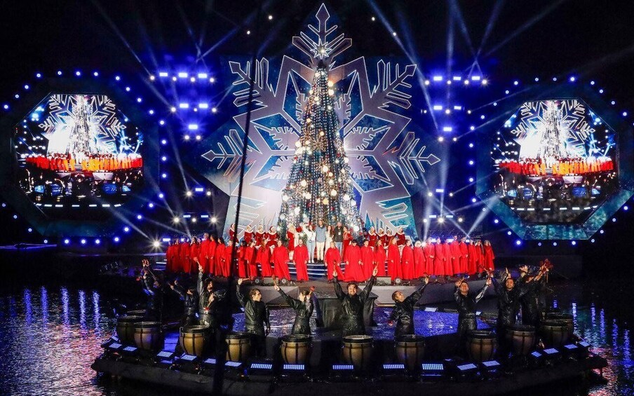 A stage with a large Christmas tree, performers in red, and a snowy backdrop. 3