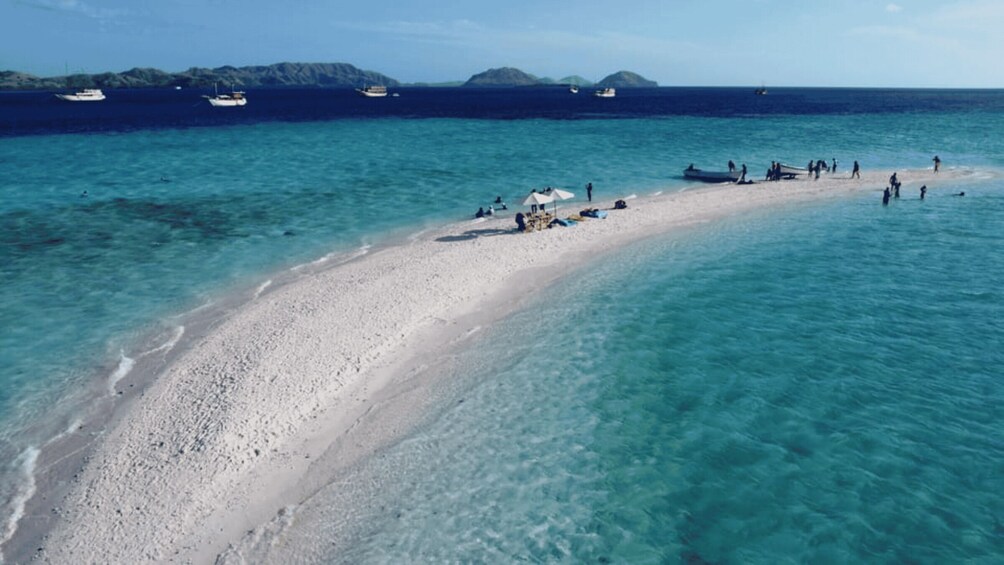 A sandy beach with clear turquoise water, boats in the distance, and a few people on the shore. 5