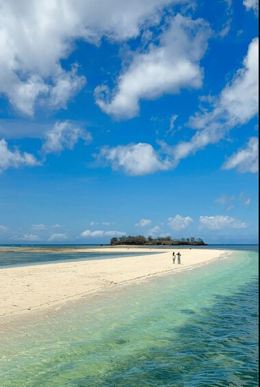A beach with clear turquoise water, a sandy shore, and a small group of people walking. 4