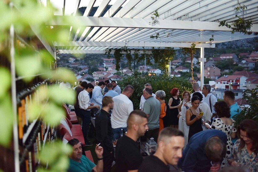 A group of people gathered under a white pergola with greenery, overlooking a residential area. 3