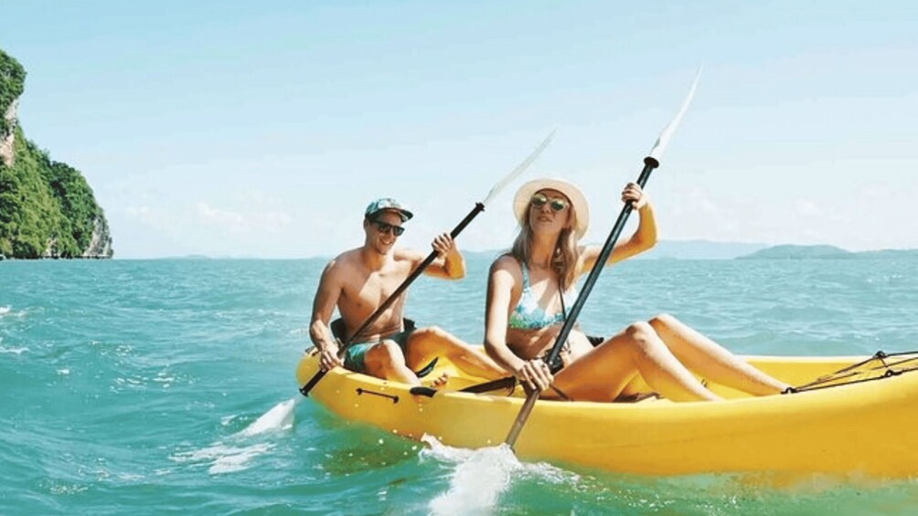 Two people in a yellow kayak on a calm sea with a green island in the background. 4