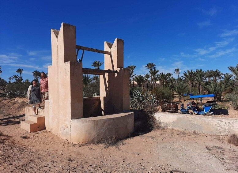 A traditional water well with a wooden frame, surrounded by palm trees and a blue vehicle. 2