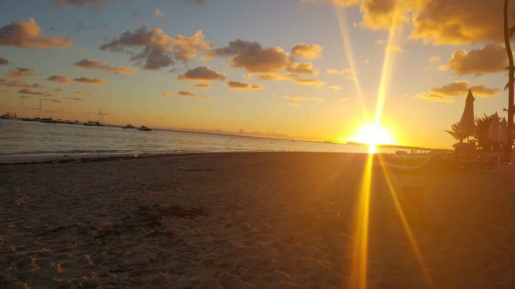 A beach at sunset with the sun low on the horizon, boats on the water, and beach umbrellas. 5