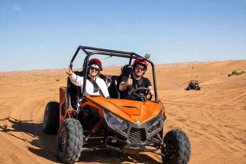 Two people in an orange off-road vehicle with a desert landscape in the background. 4