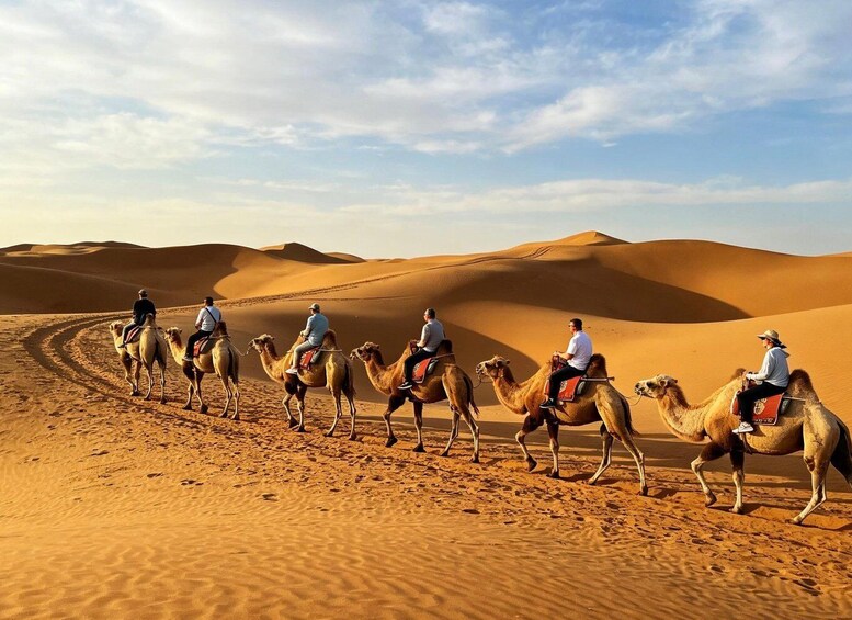 A group of people riding camels across a desert landscape with sand dunes. 1