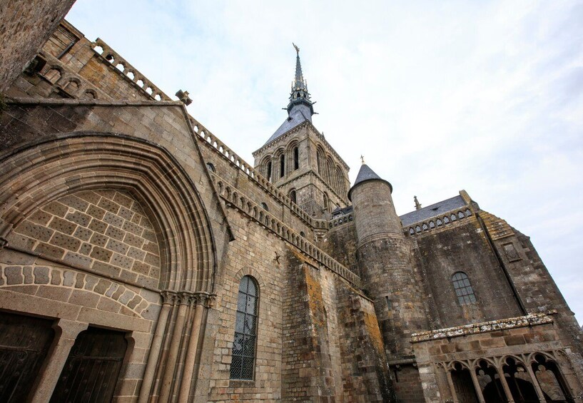 A historic stone building with a prominent arched entrance, a tall spire, and a cylindrical tower. 5