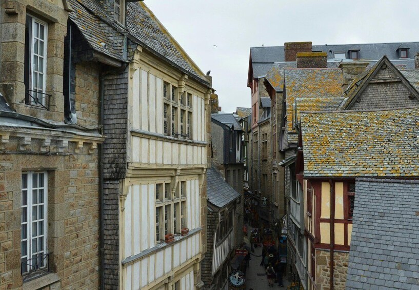 A narrow street with historic buildings, a cobblestone path, and a small crowd of people. 2