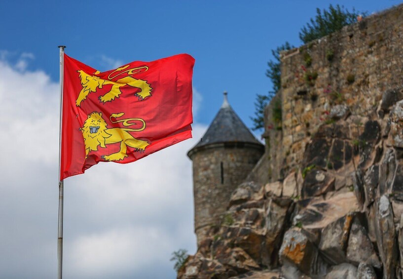A red flag with yellow lions on a flagpole, with a stone tower in the background. 1