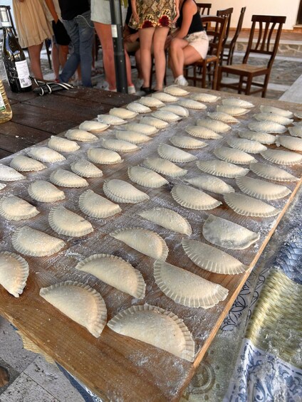 A table with numerous uncooked empanadas arranged in rows. 1