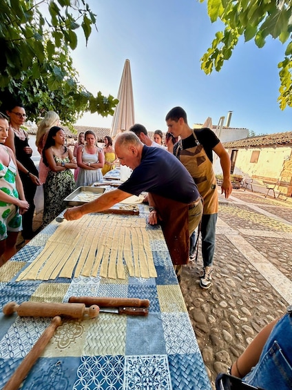 A man cutting pasta on a table outdoors with a crowd watching. 2