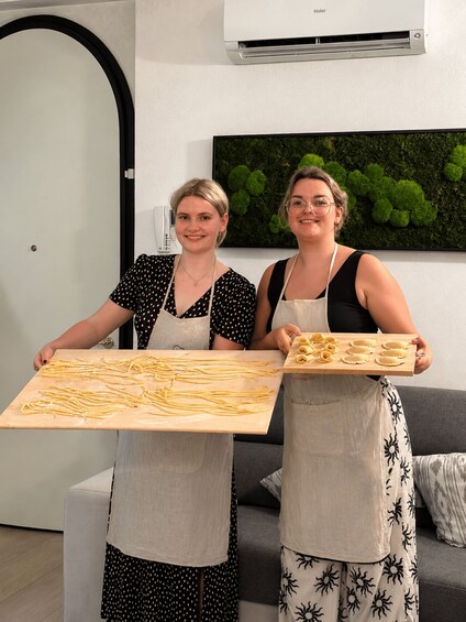 Two individuals holding wooden boards with pasta. 4