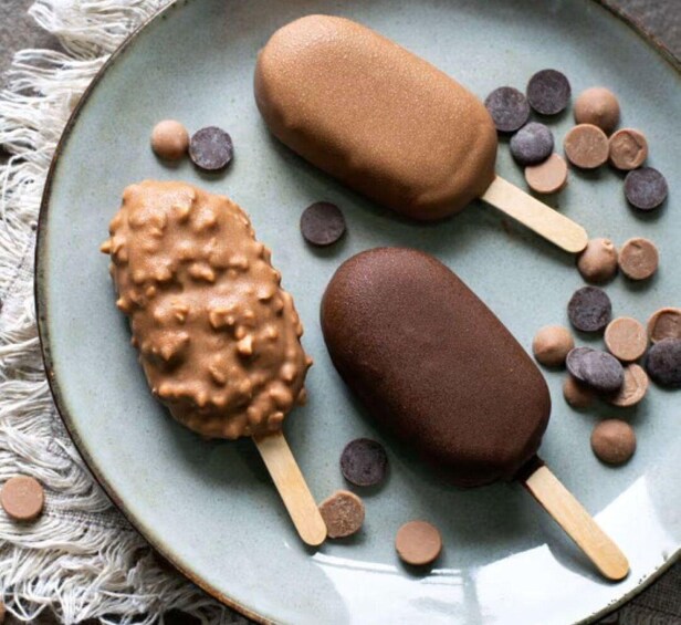 Three ice cream bars on a plate with chocolate and peanut toppings. 1