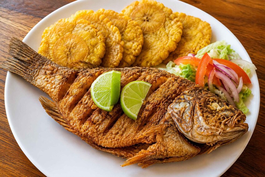 A fried fish with lime slices and fried plantains on a plate. 5