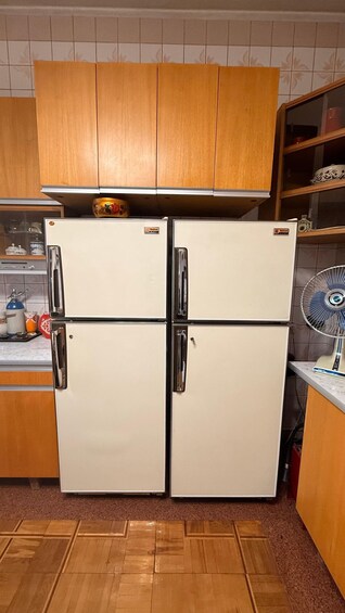 A vintage white refrigerator with black handles, placed in a kitchen with wooden cabinets and a tiled backsplash. 1