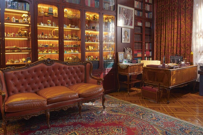 A room with a red leather sofa, wooden bookshelves, a desk, and a patterned rug. 5