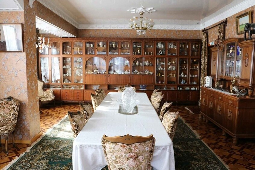 A room with a long table, ornate chairs, a chandelier, and a large cabinet filled with glassware. 3