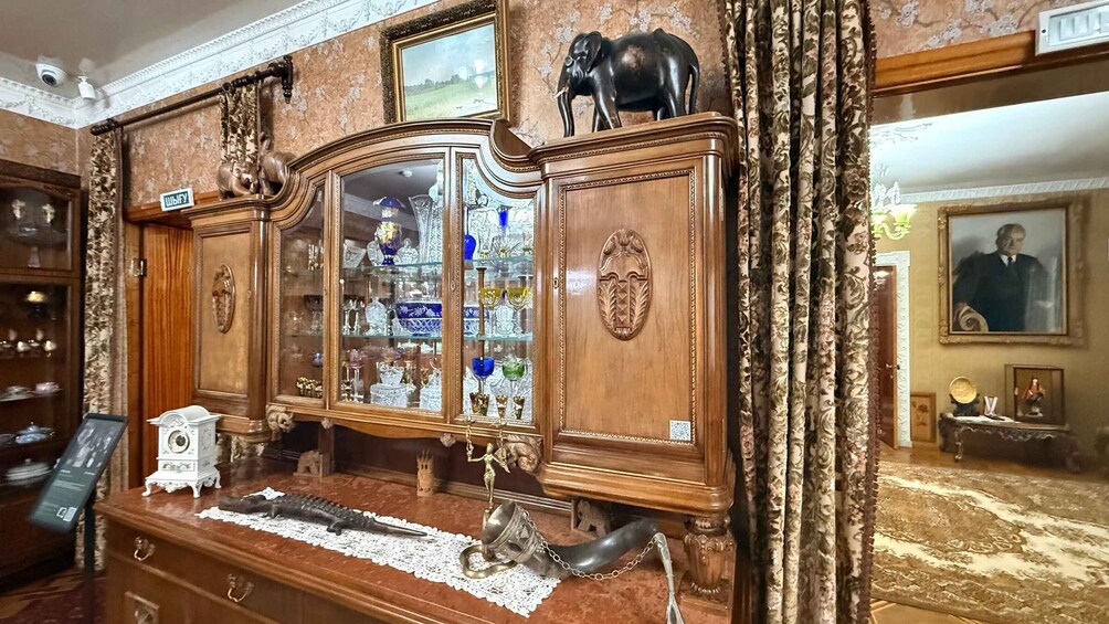 A vintage wooden cabinet with glass doors displaying glassware and figurines. 2