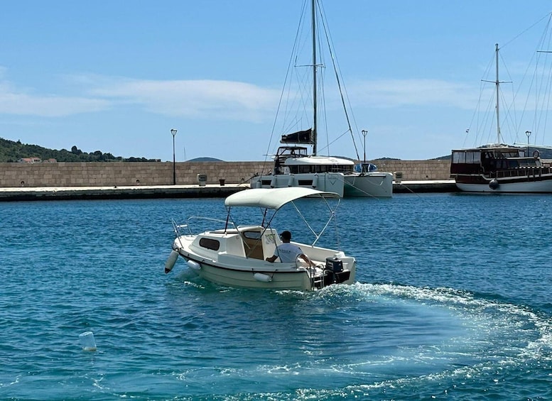A small motorboat with a canopy on the water, docked at a harbor with other boats and a stone wall in the background. 2
