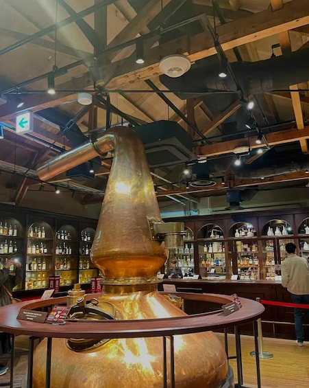 A large copper still with a long neck, surrounded by shelves of bottles, in a bar setting. 2